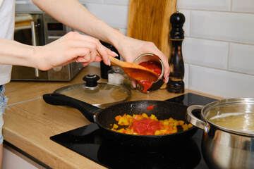 Closeup view of female hand adding canned peeled tomatoes into frying pan while preparing sauce