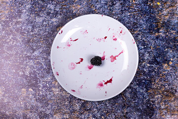 One blackberry on dirty plate with remnants of berries on dark background.