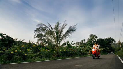 Love couple on red motorbike in white clothes to go on forest road trail trip. Two caucasian tourist woman man drive on scooter. Motorcycle rent, safety helmet, sunglasses. Asia Thailand ride tourism.