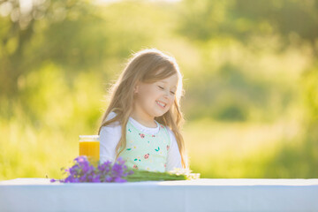 cheerful and smiling girl sits at a table on which there is orange juice