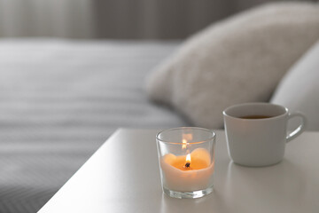 Burning candle and cup of tea or coffee stand on the bedside table.