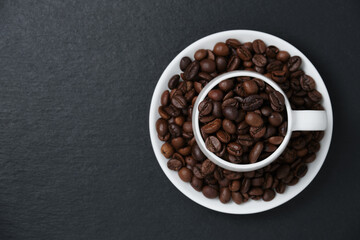 Coffee beans in a cup on a black background flat lay. Coffee beans on black slate copy space. Fragrant coffee beans in a white coffee cup top view.