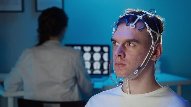 Man wearing EEG topographer for examining brain, doctor making electrogram of scalp activity. Researching of brain work using electroencephalography headset.