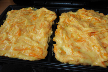 two raw Belgian waffles made from corn flour, eggs and pumpkin, lying in a waffle iron during cooking