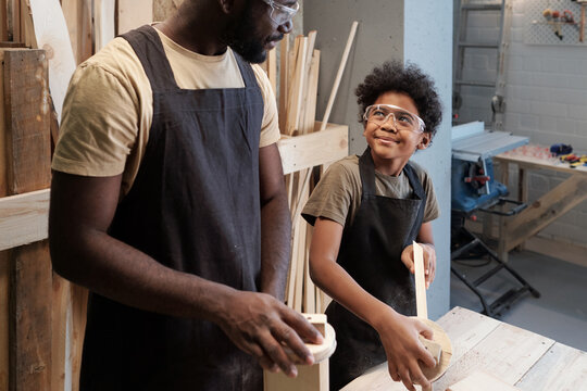 Portrait of smiling African-American boy looking at father while enjoying time together in carpentry workshop