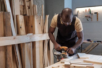 Waist up portrait of mature black carpenter sanding wood using electric tool in workshop, copy space