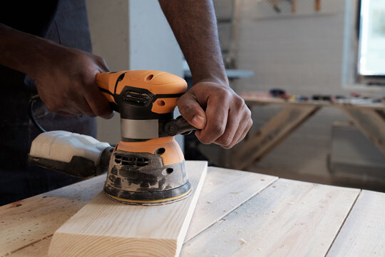 Close up of black carpenter sanding wood using electric tool in workshop, copy space