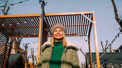 Beautiful blonde woman looks up with a smile while standing outdoors. Perfect weather for hanging out with friends. Urban art space with street food