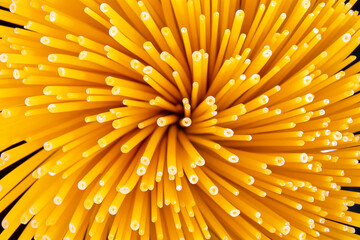Whole grain italian spaghetti pasta, selective focus. Raw spaghetti tied in a sheaf stand on a dark glass on a black background, top view, close-up.