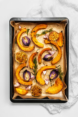 Roasted pumpkin,onion and garlic with thyme and rosemary on backing sheet. White background. Rustic food photography.  Close-up. Top view.