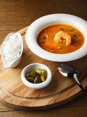 Tom Yam on a light wooden background. Serving soup in a white plate in a restaurant. Thai traditional dish with rice and shrimp. Delicious lunch. Close up, Copy space. Delicious soup with a spoon