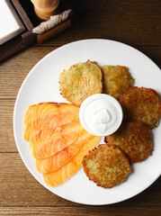 Potato pancakes with salmon. Traditional Ukrainian, Belarusian delicious food, breakfast. Fried potato pancakes with salmon and sour cream, golden crispy crust. In a white plate on a wooden background