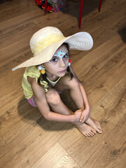 girl in a straw hat is sitting on the wooden floor hugging her knees and her eyes open