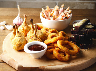 Delicious beer snacks. Crispy rings of deep-fried squid, tempura chiken, shrimp, croutons with garlic. Beautiful serving in a bar on a wooden background. Space for text. Close up. White and red sauces