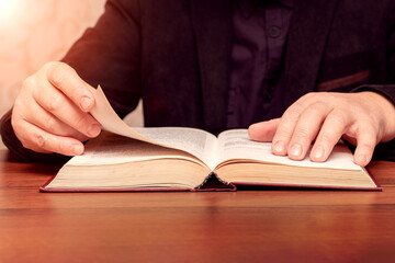 A man reads the Bible while sitting at a table. An open book in the hands of a man