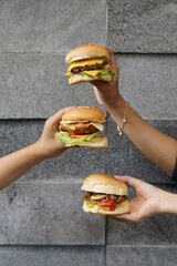 triple fresh hamburger on hand, on front of the stone wall