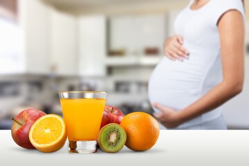 Beautiful pregnant woman standing near table with fresh vegetables and juice
