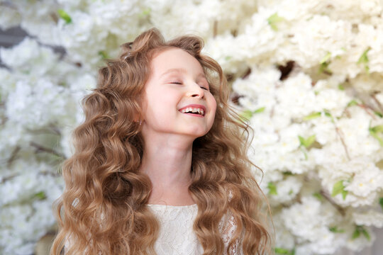 Happy beautiful cute little blonde girl child kid in blooming garden apple trees at spring sunny day, breathing deep deeply fresh air smelling enjoying smell of flowering blossom flowers, springtime