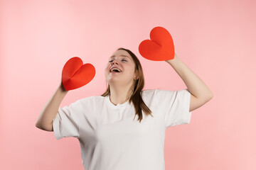 Enjoying young girl with brown hair in a white t-shirt on a pink background and red hearts. High quality photo