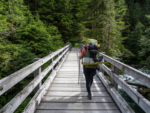 A backpacker hikes across a wooden bridge along a trail in the Quinault Rainforest in Olympic National Park.