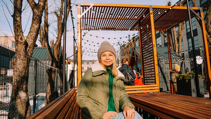 Smiling blonde woman sitting at a table in an urban space street cafe with street food. Warm winter day to meet friends