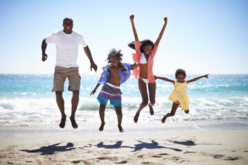 Woohoo Vacation time rocks. An excited african american family jumping into the air on the beach with a beautiful ocean in the background.