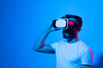 Closeup of young man wearing virtual reality goggles in modern studio with a neon light. Smartphone using with VR headset. Future technology concept.