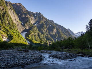 A view of the Quinault river flowing through Enchanted Valley in Olympic National Park, mountains glowing from the morning sun, the valley in shade.