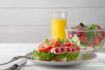 Sandwich with sausage and tomatoes, with salad and orange juice. European breakfast.
