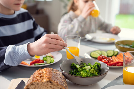 Breakfast at home: children drinking orange juice and nailing fresh green broccoli on a fork
