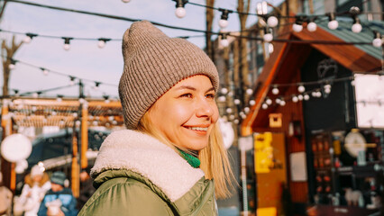 Young blonde at the European street food fair. She is happy and smiling on a sunny winter day. Blurred background of various street food sales points