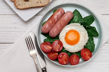 Fried eggs with sausages, spinach, tomatoes, toast and orange juice on a white wooden background. European breakfast.