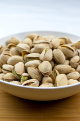 A white bowl of pistachios on a bamboo board with a white background.  Copy space.