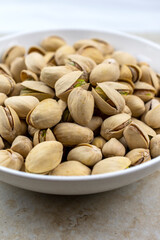 Side view of a white bowl of pistachios on a tile surface.