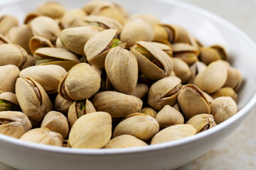 Side view of a white bowl of pistachios on a tile surface.