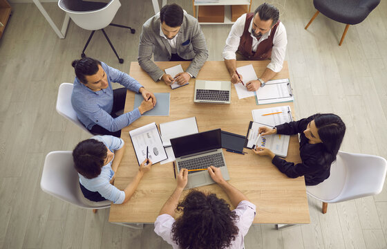 View from above of a group of business people having a meeting around the office table. Top view of a professional sales team discussing work projects and taking decisions. Teamwork concept