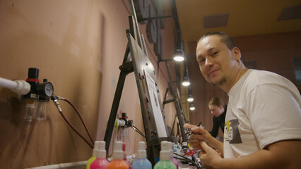 Man artist learns to paint with airbrush with acrylic dye, paper and easel. Indoors. Concept modern...