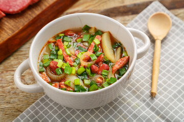 Bean soup with smoked meats and greens of Jewish cuisine cholit in a tureen and a wooden spoon.