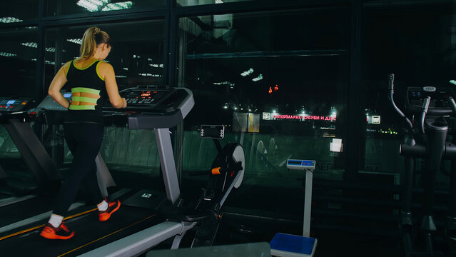 Fit Athletic Woman Running on the Treadmill, Doing Her Fitness Exercise. Muscular Women Activity Training in Modern Gym. Sports People Workout in Running track Fitness Center. Side View Slow Motion