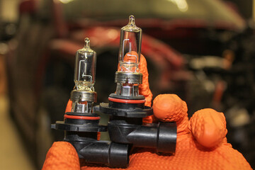 Car light bulbs in the hand of a man with orange gloves. Car repair. A mechanic in orange rubber...
