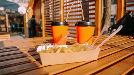 Fast food. Two orange paper cups and french fries with sauce on wooden table. Food concept at the street food court outside