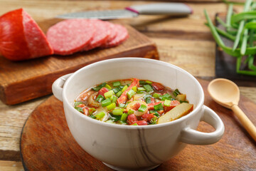 Bean soup of Jewish khni cholit on a round stand, green onions, sausage and bread nearby.