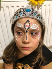 little  girl with a diadem on her head is  looking away. princess with a openwork paint on her face