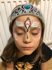 little fairy girl with a diadem on her head is  closing her eyes. princess with a  tracery paint on her face and tiara