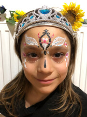 little girl with a tiara on her head is smiling. princess with a pattern on her face