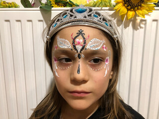 little sad girl with a diadem on her head is  looking away. dream princess with a art painting on her face
