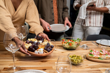 Close-up of woman putting the appetizers on dining table with her friends helping her, they arranging dinner party