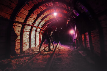 Tired young miner in an old coal mine works with a jackhammer. A miner in a protective suit with a...