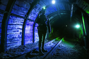 A tired young miner in an old coal mine stands with a jackhammer on his shoulder. A miner in a...