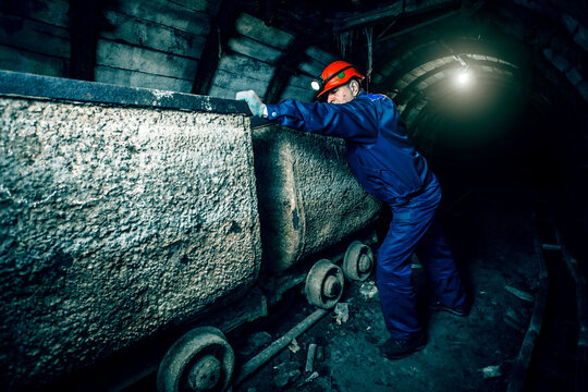 Tired miner in an old coal mine in the process of working. A miner in a blue protective suit with an orange helmet on his head. Copy space.